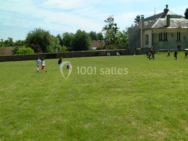 Des enfants jouent sur une grande pelouse devant un bâtiment ancien entouré d'arbres et d'un mur en pierre.