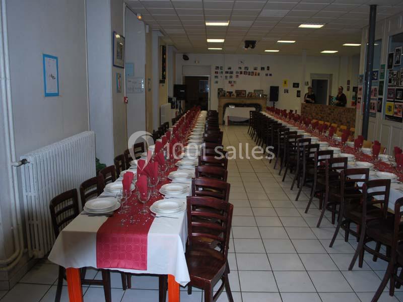 Salle de réception avec de longues tables dressées, nappes blanches et rouges, alignées pour un grand événement.