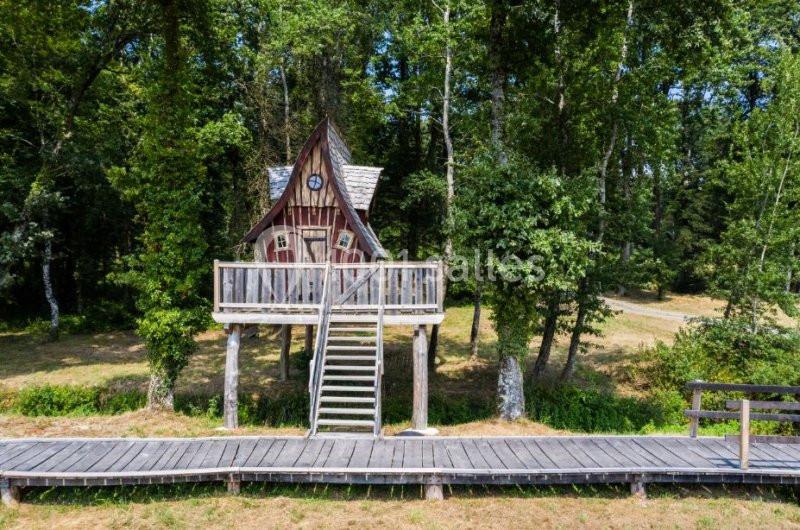 Cabane en bois sur pilotis avec escalier, entourée d'arbres dans un cadre naturel.