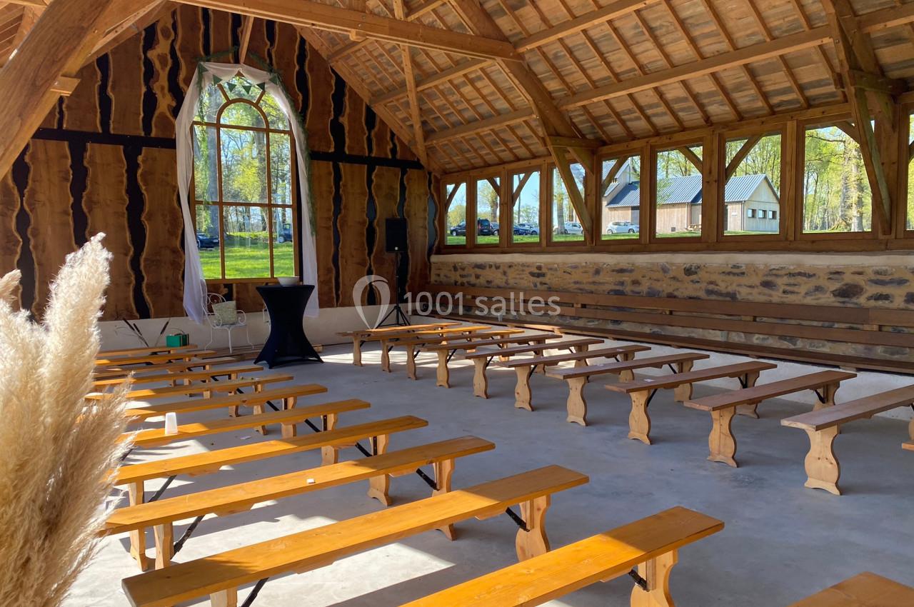 Salle en bois avec bancs alignés, grandes fenêtres laissant entrer la lumière et vue sur l'extérieur verdoyant.