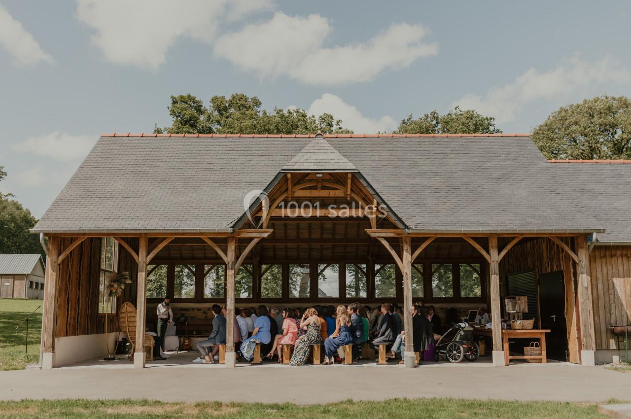 Un groupe de personnes assises sous un grand abri en bois ouvert, entouré de verdure et de ciel dégagé.