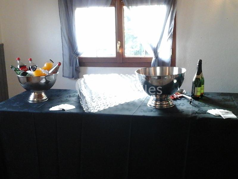 Table avec nappes noires, seaux contenant bouteilles et fruits, flûtes en verre alignées devant une fenêtre.