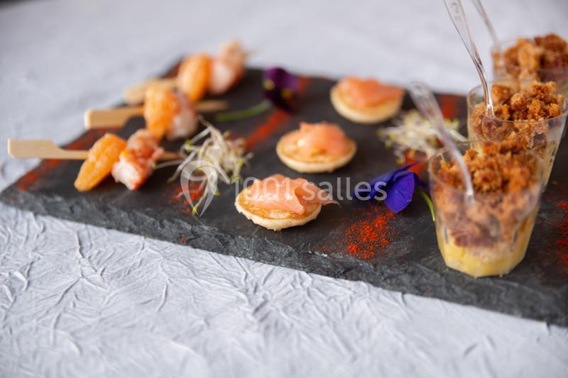 Assortiment de bouchées apéritives sur une ardoise, incluant crevettes, saumon fumé et verrines gourmandes.