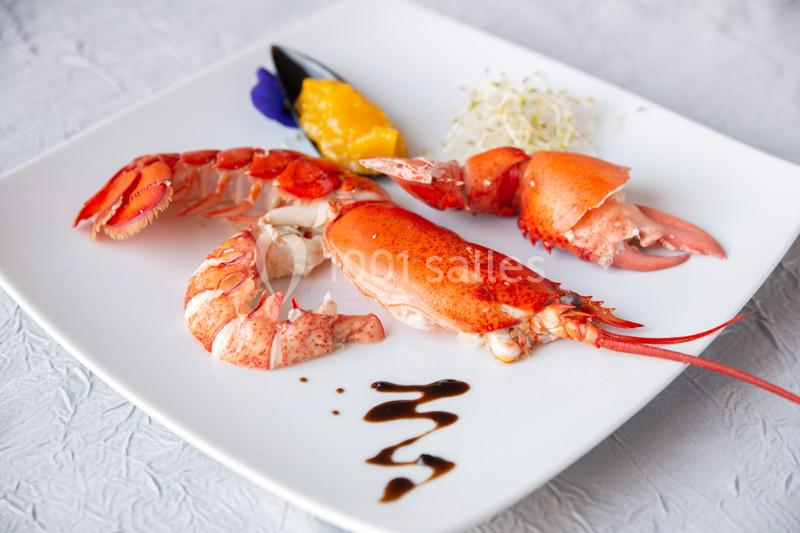 Assiette de homard dressée avec une purée de mangue, des pousses germées et un filet de sauce balsamique.