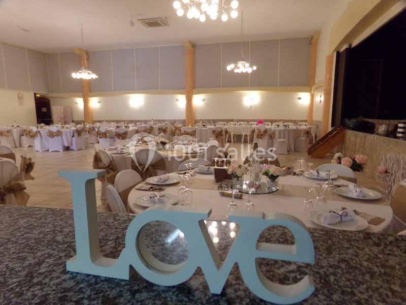 Salle de réception décorée pour un mariage, avec tables dressées et un mot ’Love’ en premier plan.