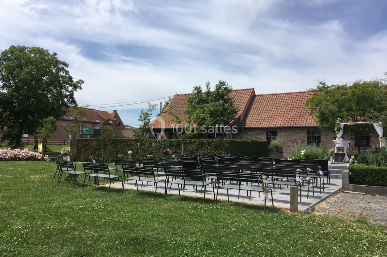 Chaises disposées en extérieur devant une petite bâtisse en briques avec toit en tuiles, entourée de verdure.