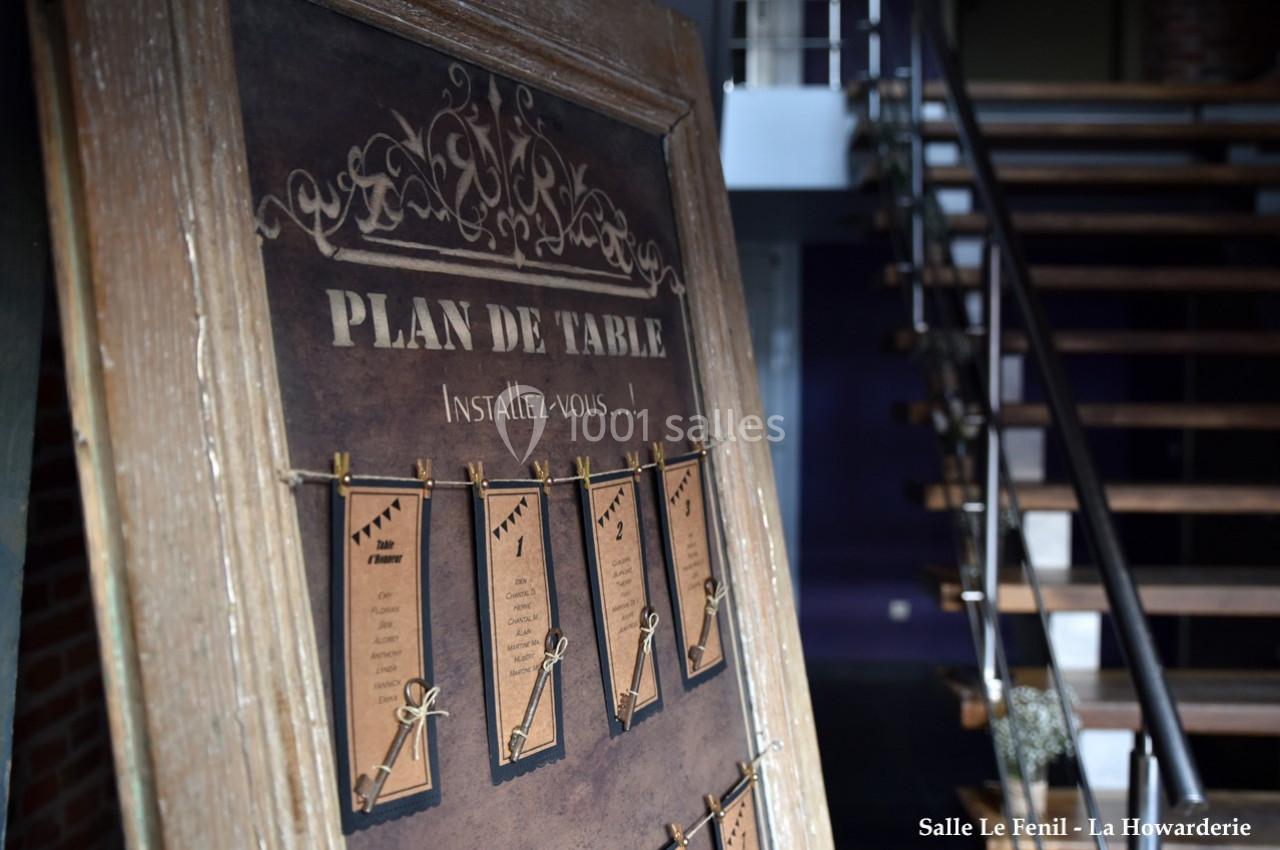 Plan de table affiché sur un panneau en bois avec des cartes suspendues, dans un espace intérieur avec escalier en arrière…