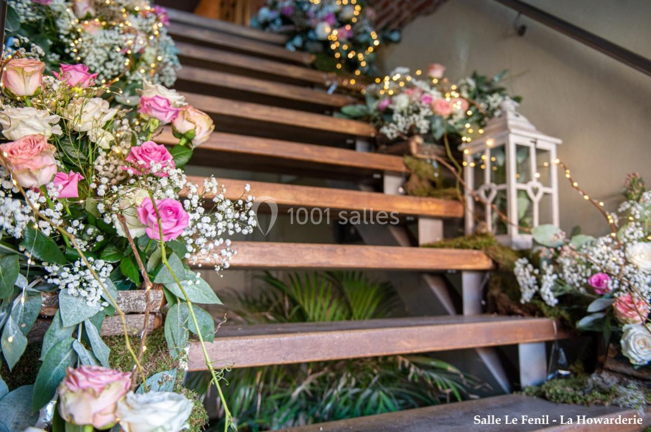 Escalier décoré de fleurs roses et blanches, feuillages et guirlandes lumineuses, avec une lanterne blanche.
