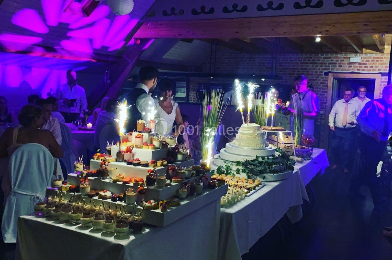 Table de desserts variés avec gâteaux, verrines et décorations lumineuses dans une salle de réception festive.