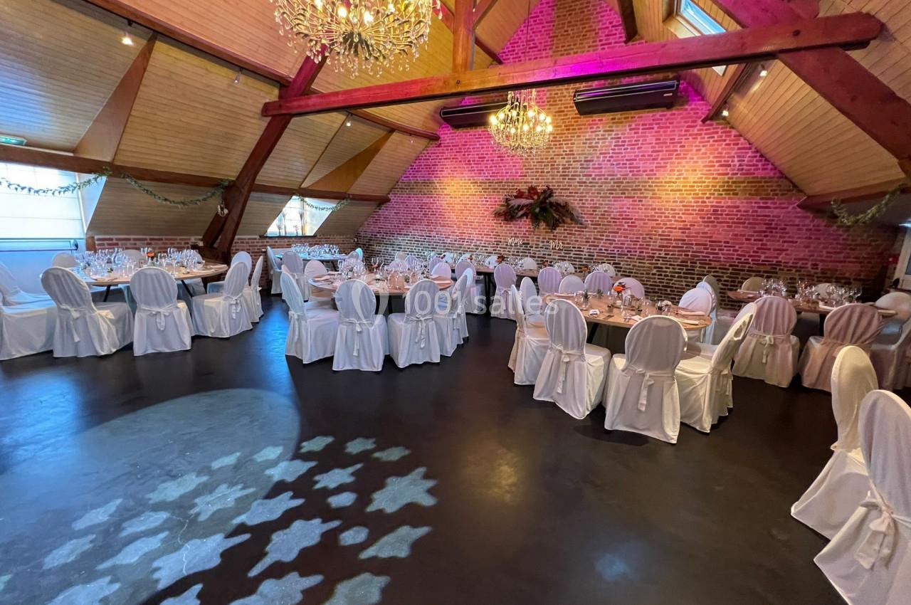 Salle de réception décorée avec des tables dressées, des chaises blanches et des lustres suspendus sous un plafond en bois.