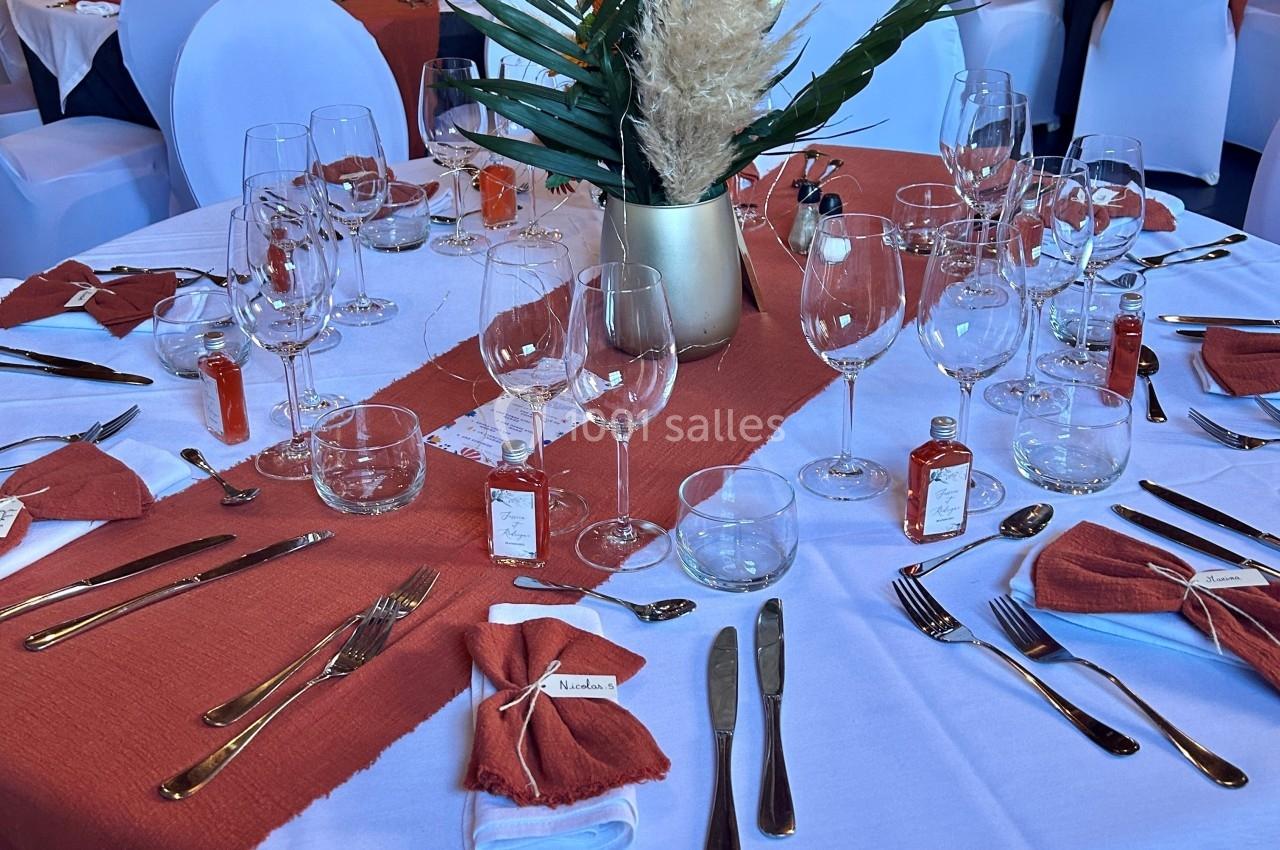 Table de réception élégamment dressée avec nappes blanches, chemins de table rouges, couverts et verres disposés.