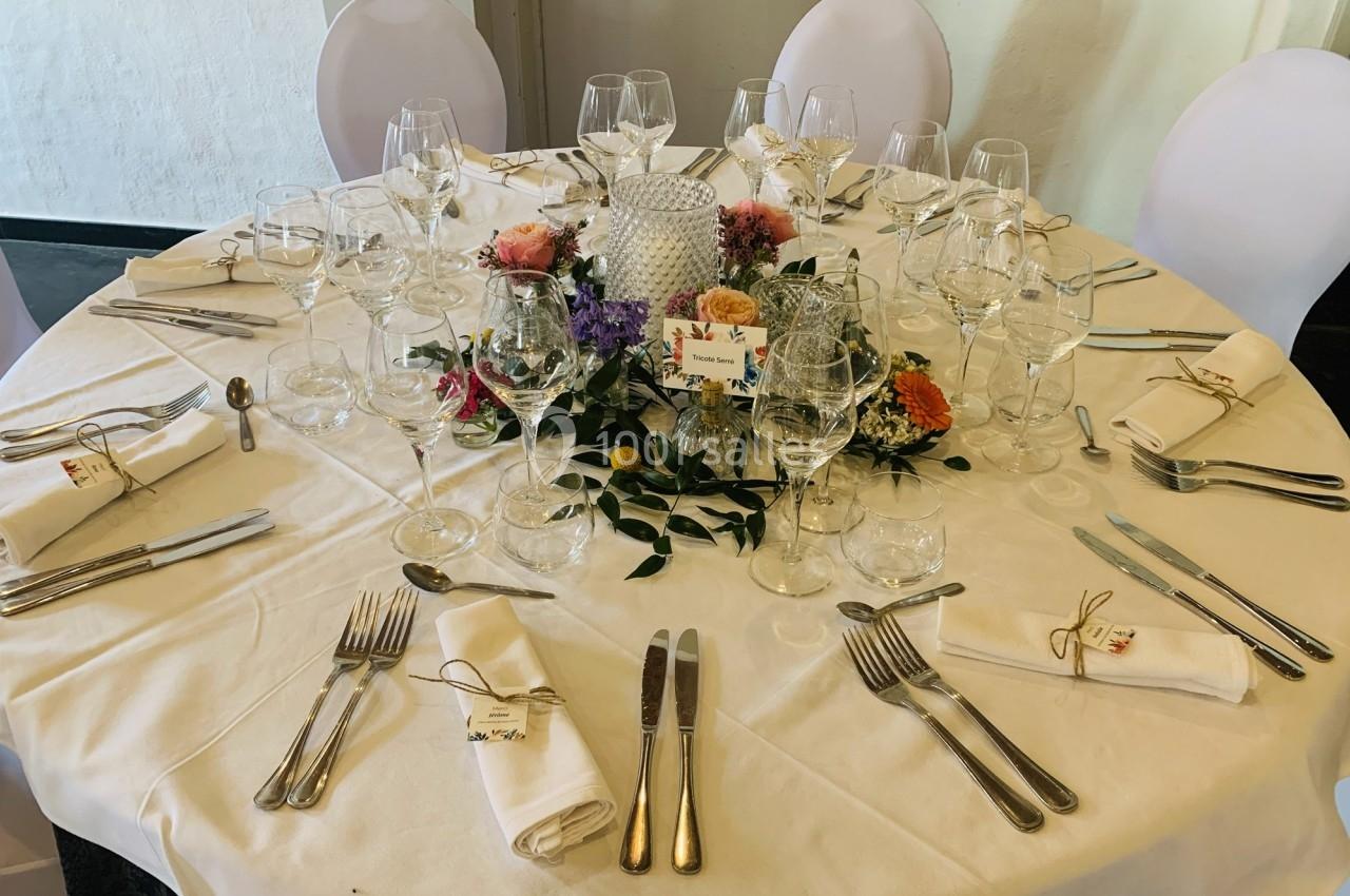 Table ronde élégamment dressée avec nappes blanches, couverts, verres, serviettes pliées et centre de table floral.