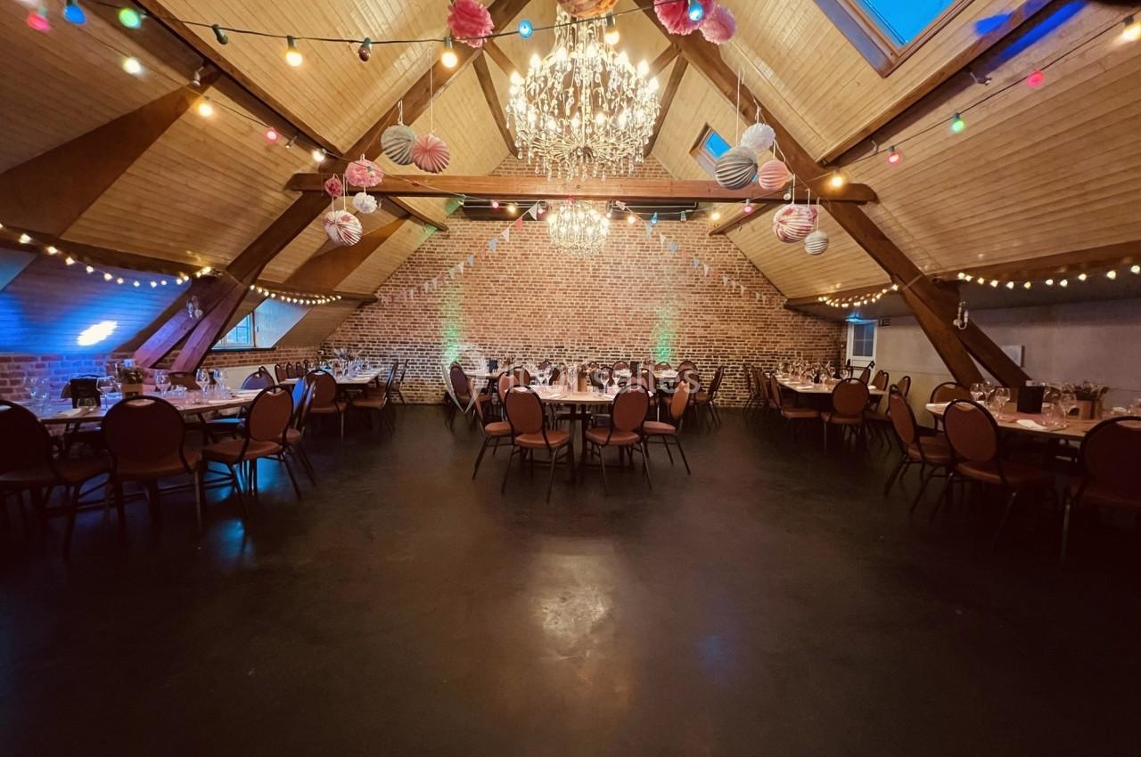 Salle de réception décorée avec des guirlandes lumineuses, des suspensions colorées et des tables dressées.