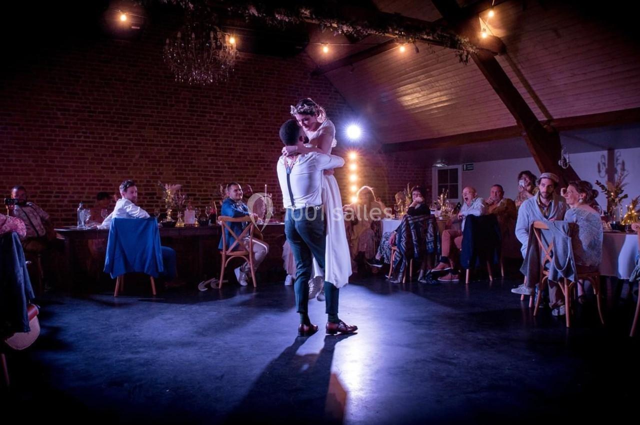 Un couple danse au centre d'une salle éclairée, entouré d'invités assis à des tables.