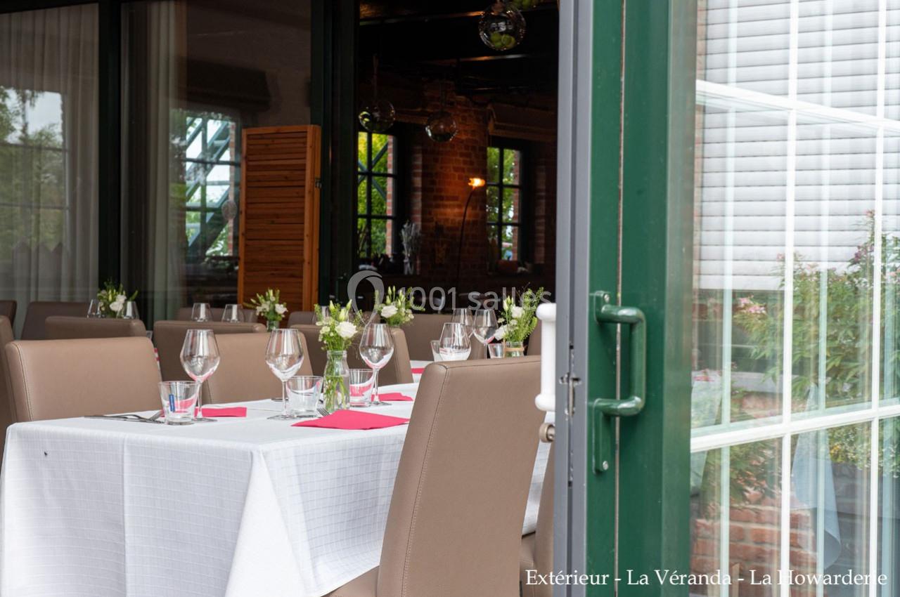Table dressée avec nappes blanches, verres et fleurs, située près d'une baie vitrée ouverte donnant sur un espace verdoyant.