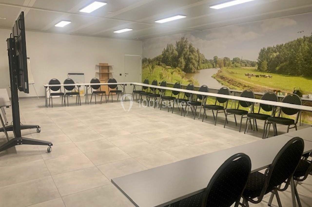 Salle de réunion lumineuse avec des tables disposées en U, des chaises noires et un mur décoré d'une photo de paysage…