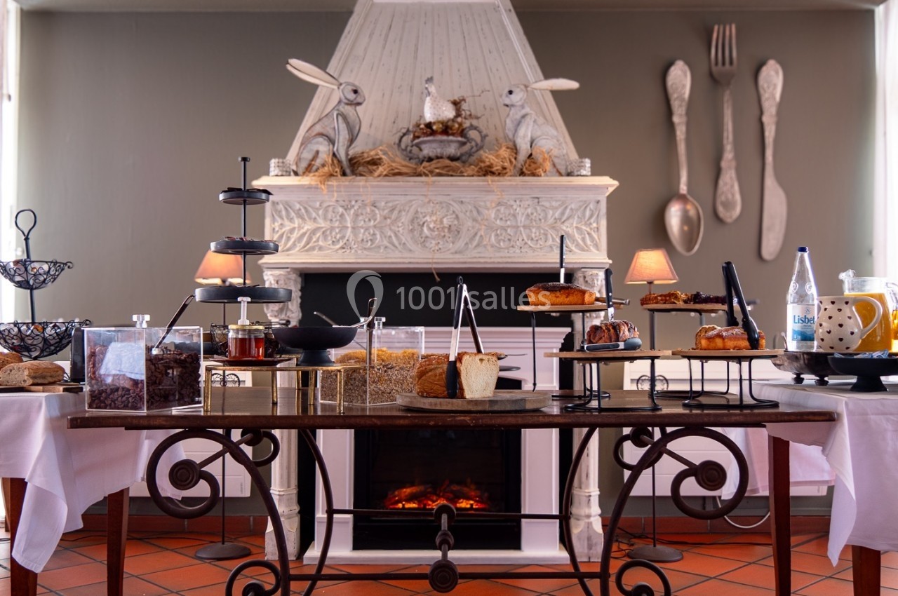 Table garnie de desserts variés devant une cheminée décorée avec des lapins et des ustensiles géants accrochés au mur.