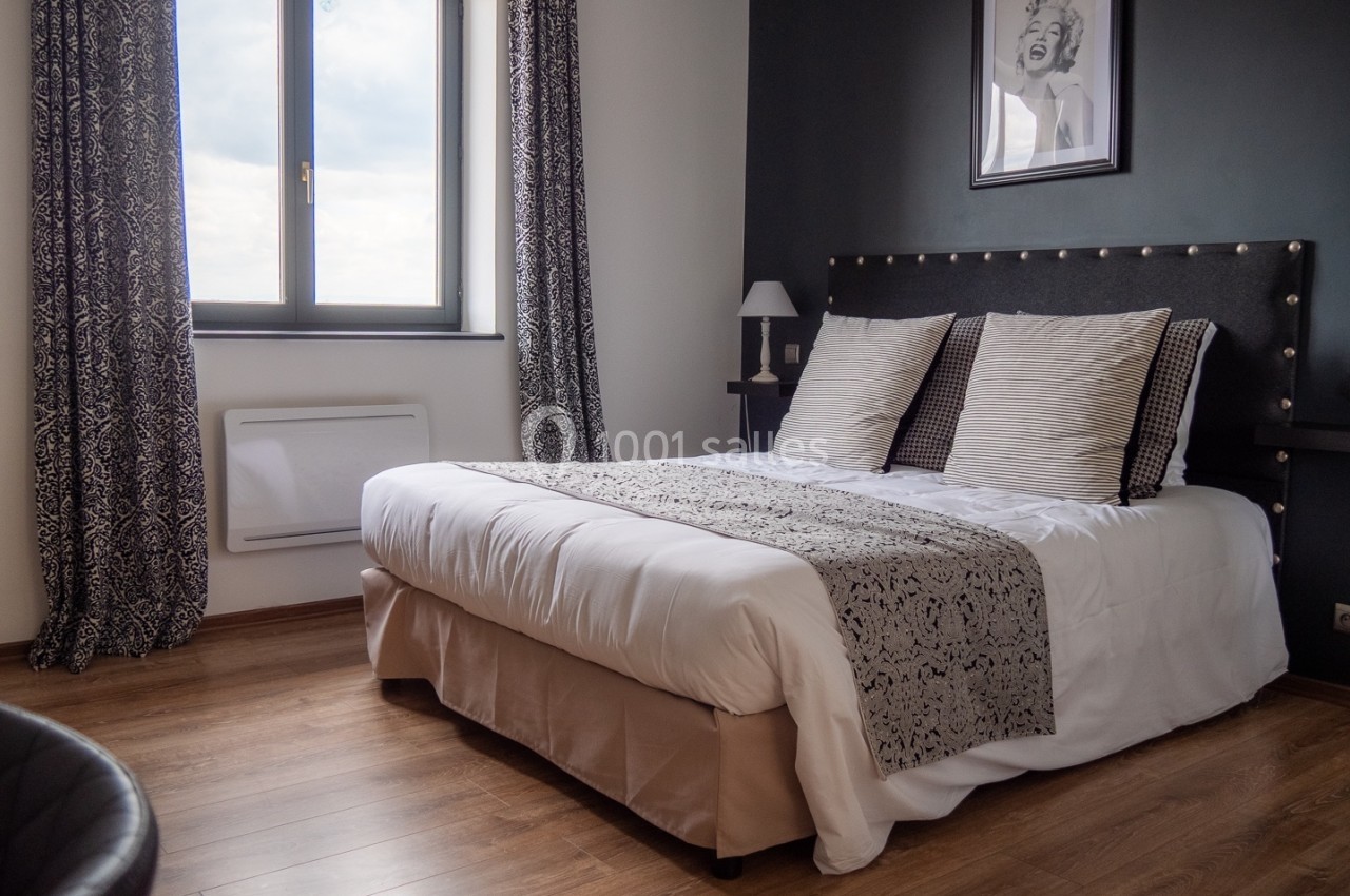Chambre avec lit double, parquet, murs sombres, rideaux à motifs, et fenêtre laissant entrer la lumière naturelle.