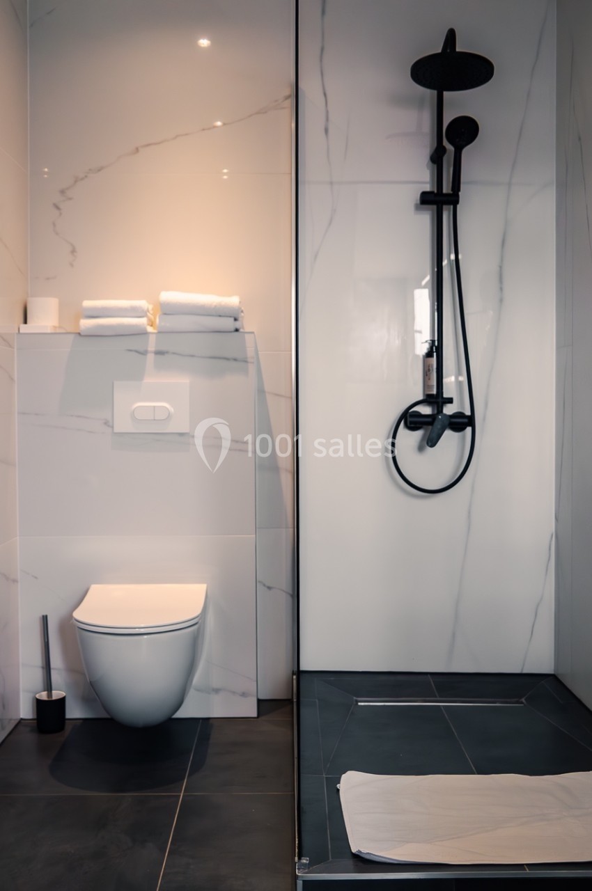 Salle de bain moderne avec toilettes suspendues, douche à l'italienne noire et murs en marbre clair.