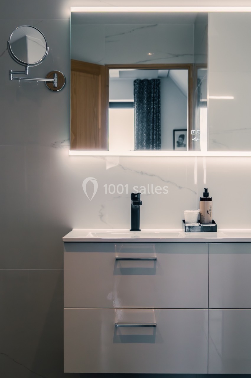 Meuble de salle de bain moderne avec deux robinets, miroir éclairé et accessoires de toilette minimalistes.
