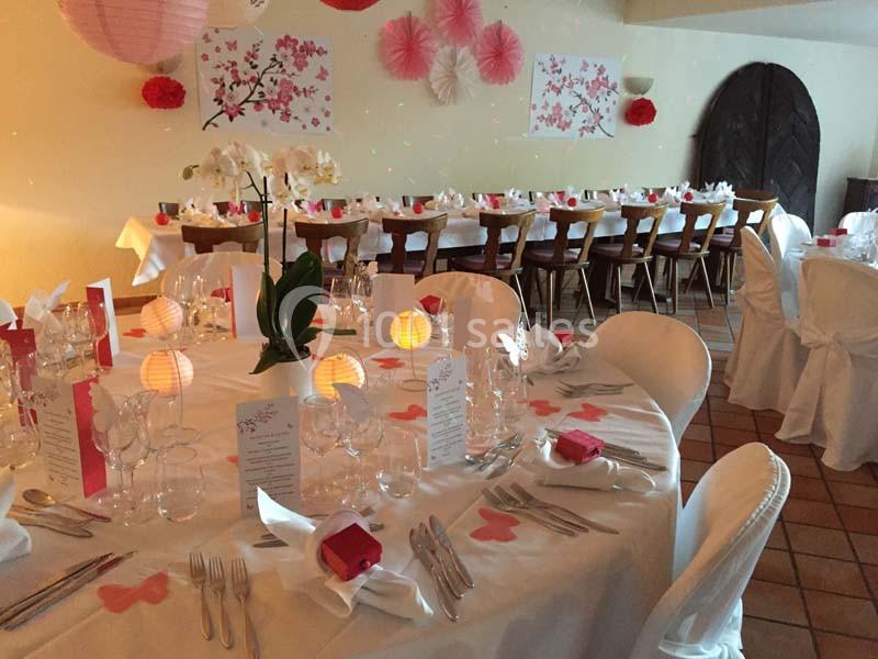 Salle décorée pour un événement avec tables dressées, nappes blanches, lanternes et motifs floraux roses.