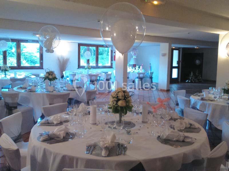 Salle de réception décorée avec des tables rondes, nappes blanches, ballons transparents et arrangements floraux.