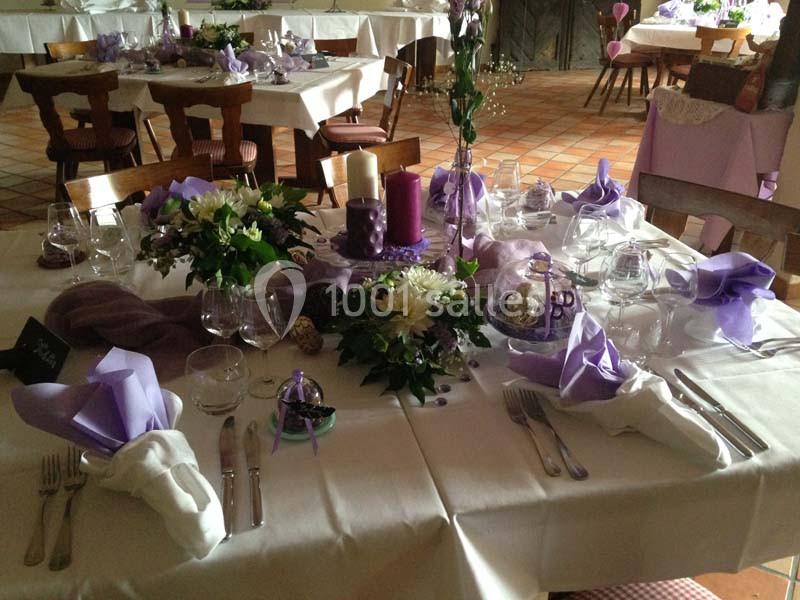 Table décorée pour un événement avec nappes blanches, serviettes violettes, bougies et compositions florales.