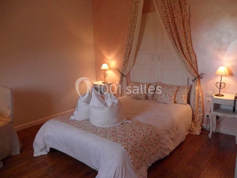 Lit double avec draps blancs et coussins fleuris, encadré par des rideaux assortis, dans une chambre lumineuse au sol en…