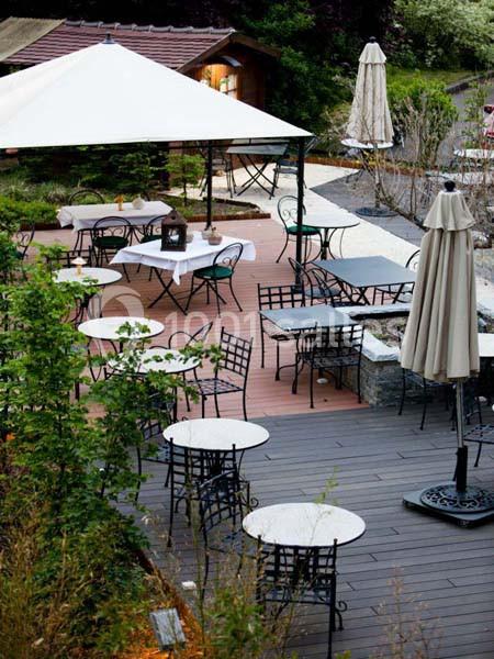 Terrasse extérieure avec tables et chaises en fer forgé, partiellement ombragée par un grand parasol blanc.