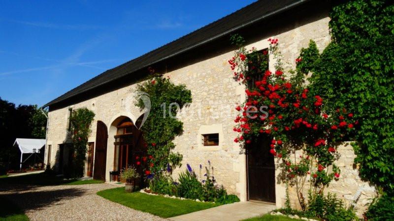 Façade en pierre d'une maison avec des rosiers grimpants et une allée en gravier bordée de verdure.