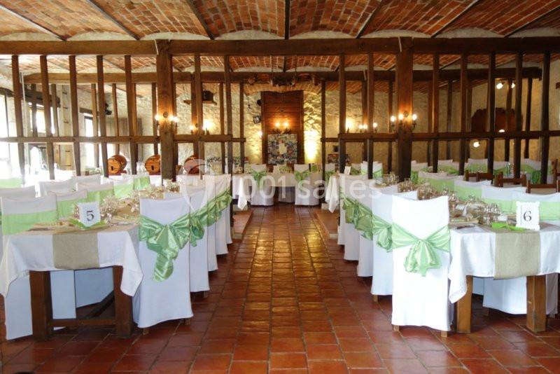 Salle de réception décorée avec des tables dressées, nappes blanches et nœuds verts sur les chaises.