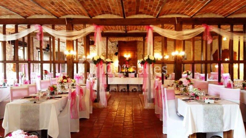 Salle de réception décorée avec des nappes blanches, des chaises ornées de rubans roses et des arrangements floraux.