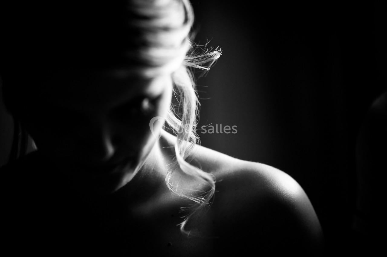 Portrait en noir et blanc d'une femme avec des cheveux blonds bouclés, partiellement éclairée dans l'obscurité.