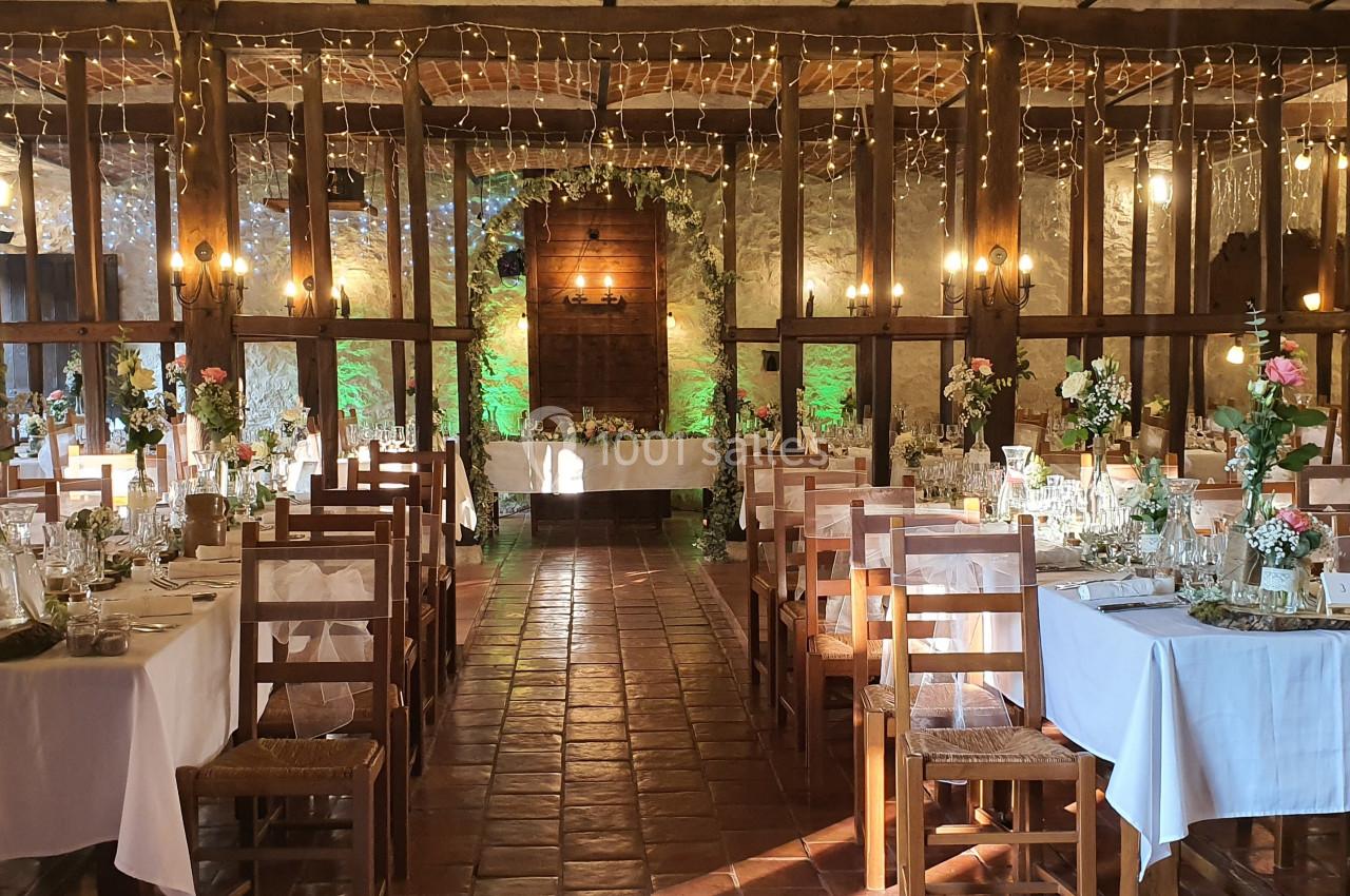Salle de réception décorée avec des tables dressées, des fleurs et des guirlandes lumineuses suspendues.