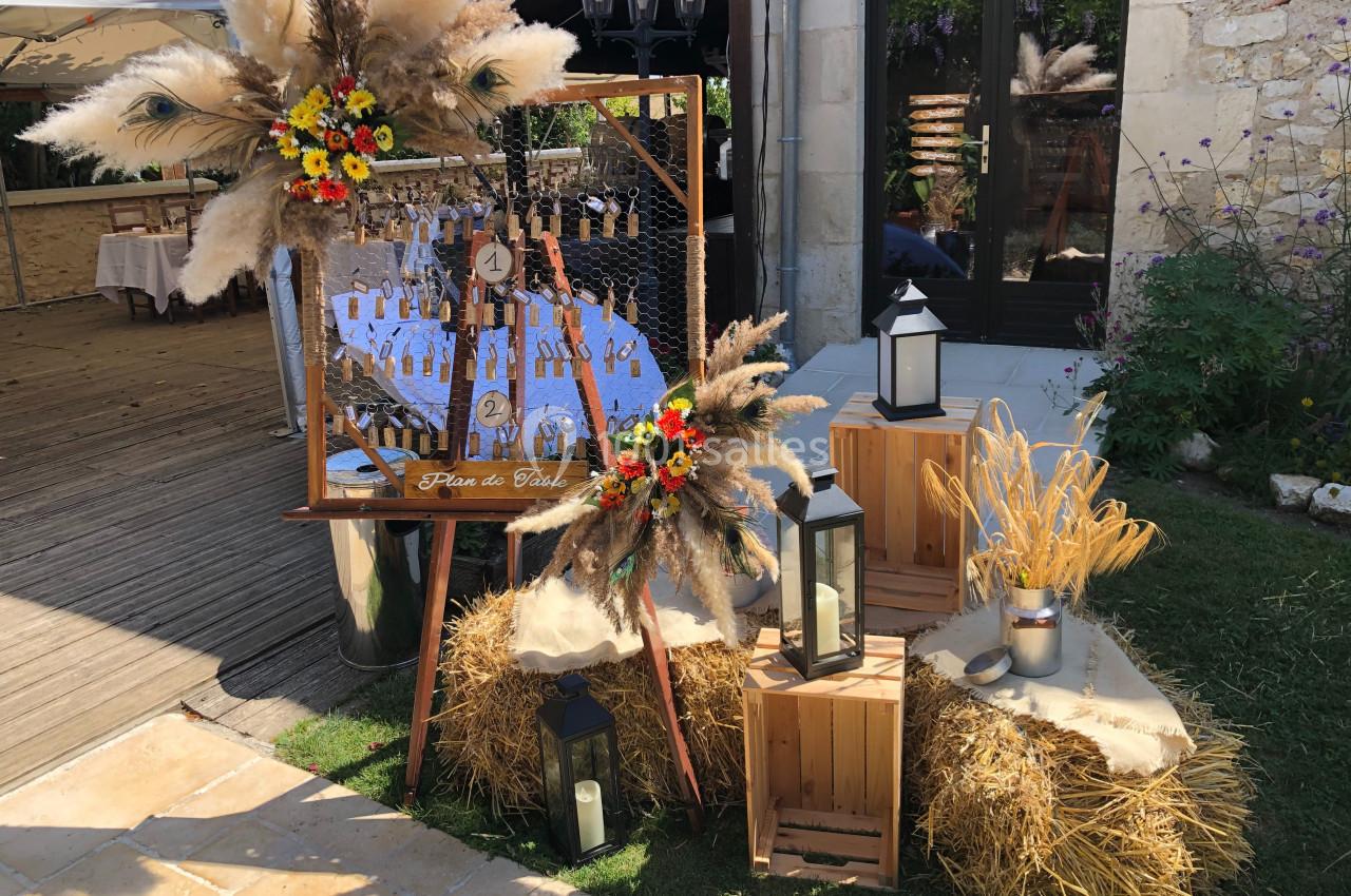 Plan de table champêtre avec décorations en bois, fleurs séchées, lanternes et bottes de paille dans un cadre extérieur.