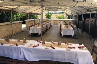 Tente rouge et blanche abritant des tables dressées avec nappes et décorations pour un repas en extérieur.