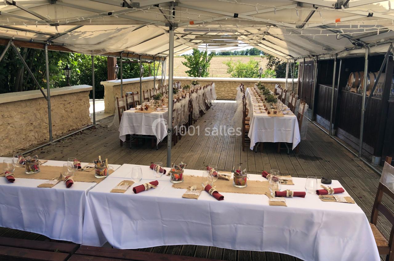 Tables dressées avec nappes blanches, décorations et couverts, sous une tente ouverte dans un cadre extérieur.