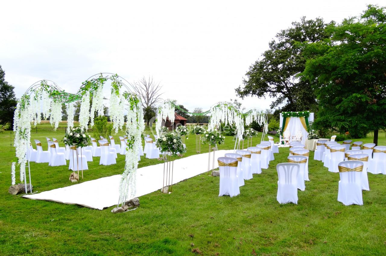 Allée centrale décorée de fleurs blanches et chaises alignées pour une cérémonie en plein air sur une pelouse verte.