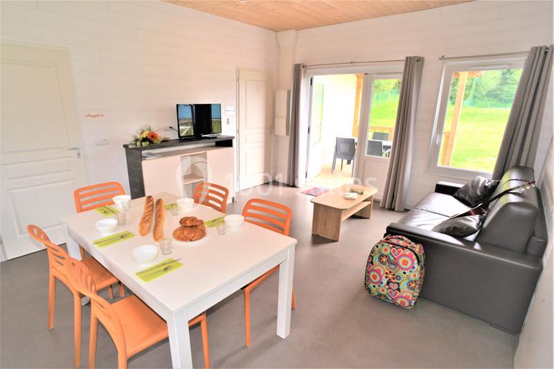 Salle de séjour lumineuse avec table dressée, canapé, télévision et vue sur une terrasse donnant sur un espace vert.