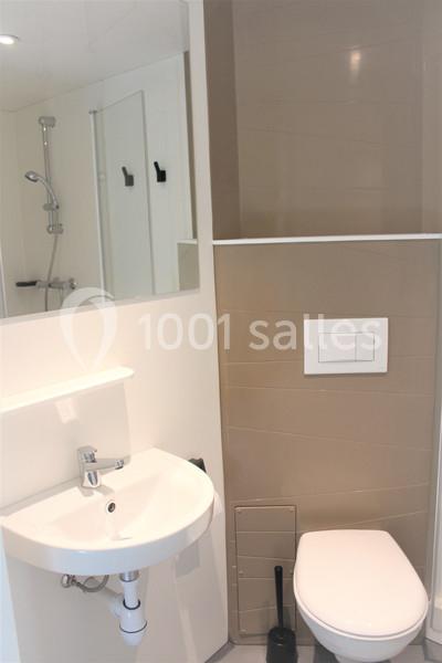 Salle de bain compacte avec lavabo, miroir, toilettes suspendues et douche en arrière-plan.