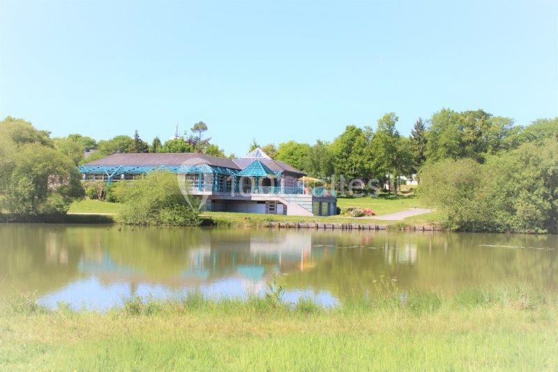 Bâtiment avec une structure bleue situé au bord d'un étang entouré de verdure sous un ciel dégagé.