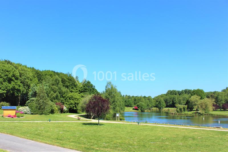 Vue d'un parc avec pelouse, arbres, sentiers et un étang sous un ciel bleu clair.