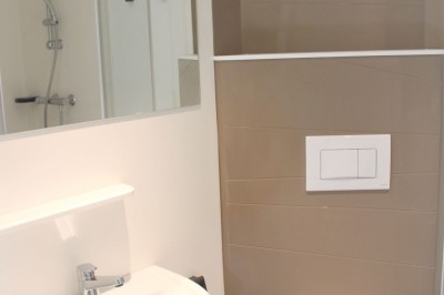 Salle de bain moderne avec lavabo, miroir, toilettes suspendues et douche en arrière-plan.