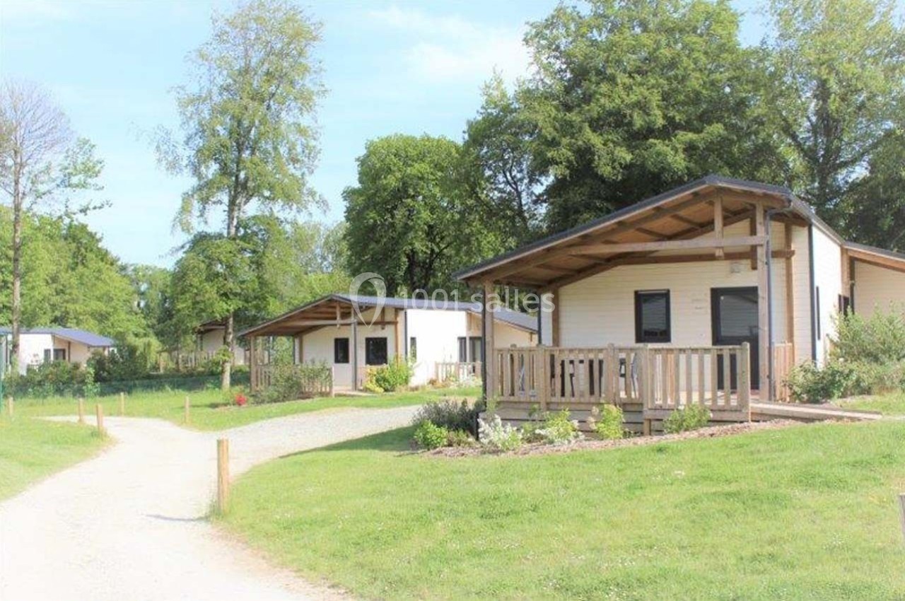 Chalets en bois avec terrasses, entourés de pelouses et d'arbres, dans un cadre naturel et ensoleillé.