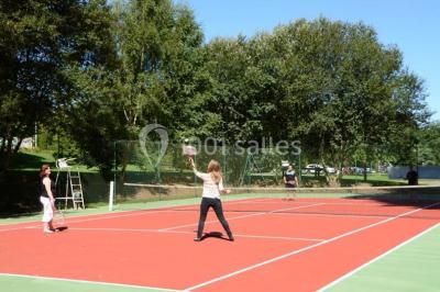 Deux personnes jouent au tennis sur un court extérieur entouré d'arbres par une journée ensoleillée.