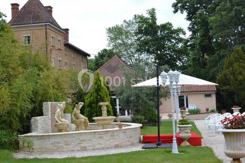 Jardin avec fontaine ornée de statues, lampadaires blancs, chaises disposées et bâtiments en arrière-plan.