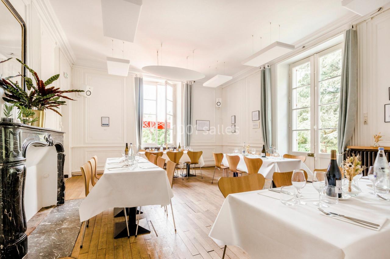Salle de restaurant lumineuse avec tables dressées, grandes fenêtres, parquet en bois et décoration épurée.