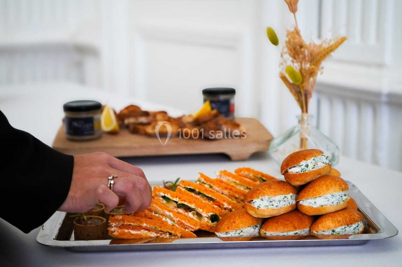 Plateau de sandwichs garnis de saumon et de fromage frais, avec une main prenant un amuse-bouche.