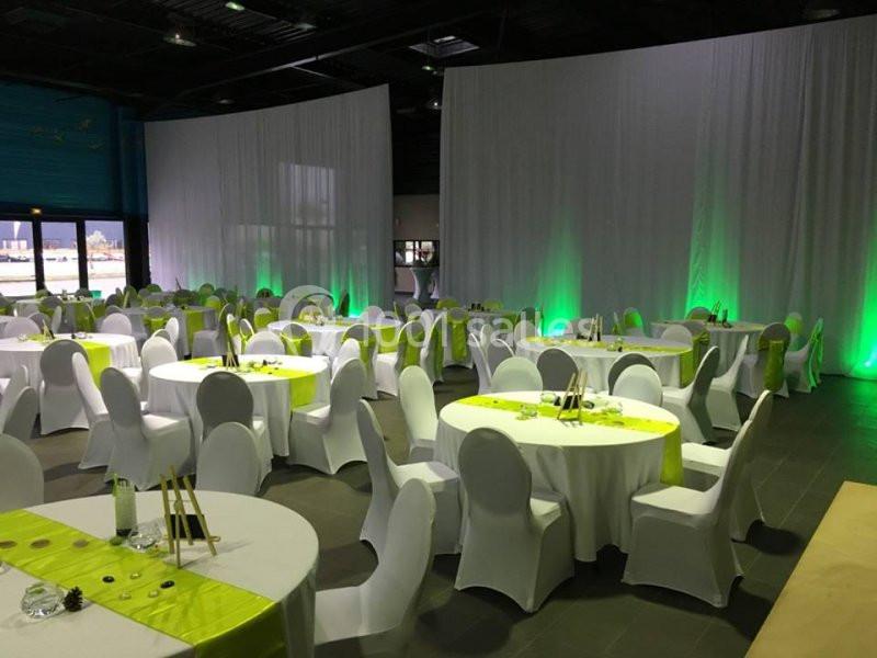 Salle de réception décorée avec des tables rondes, nappes blanches et chemins de table verts, éclairage d'ambiance.