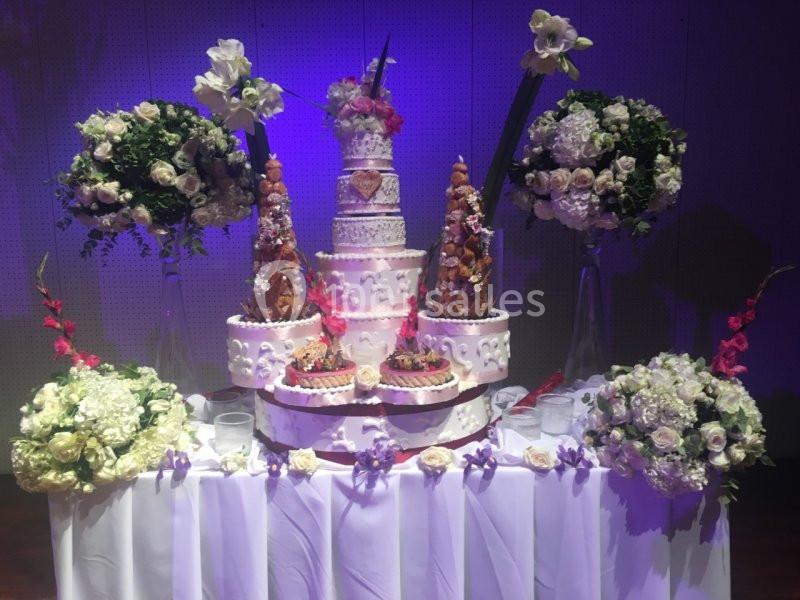 Table décorée avec un grand gâteau de mariage central, entouré de pièces montées et de bouquets de fleurs blanches et…